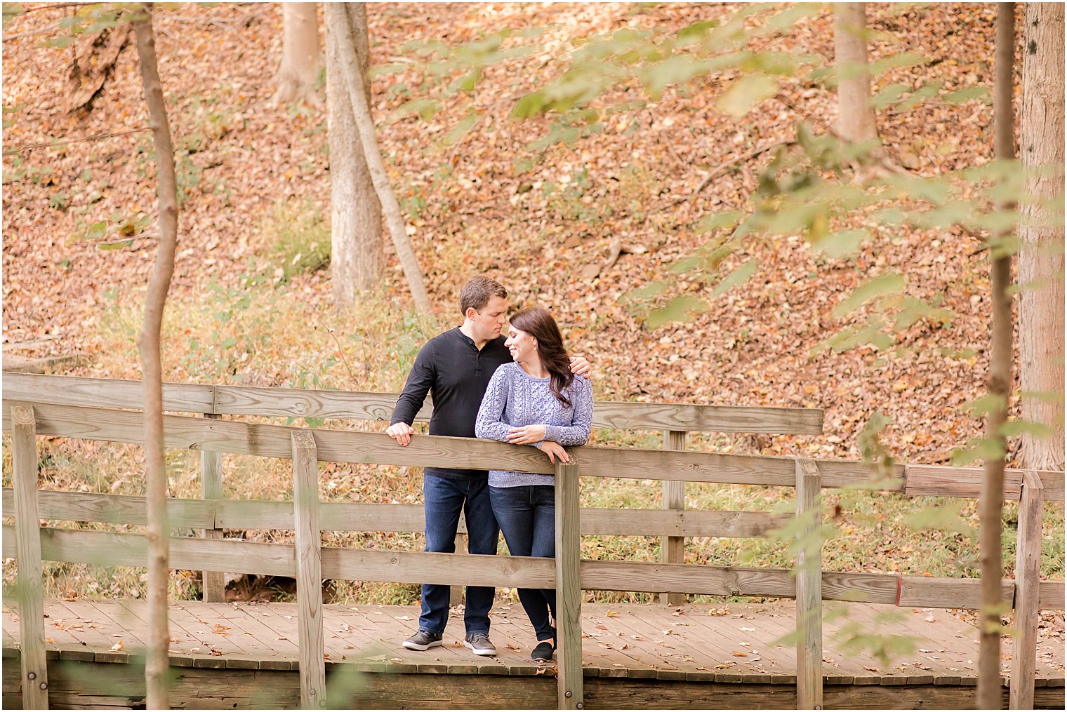 engaged couple stands together on wooden bridge