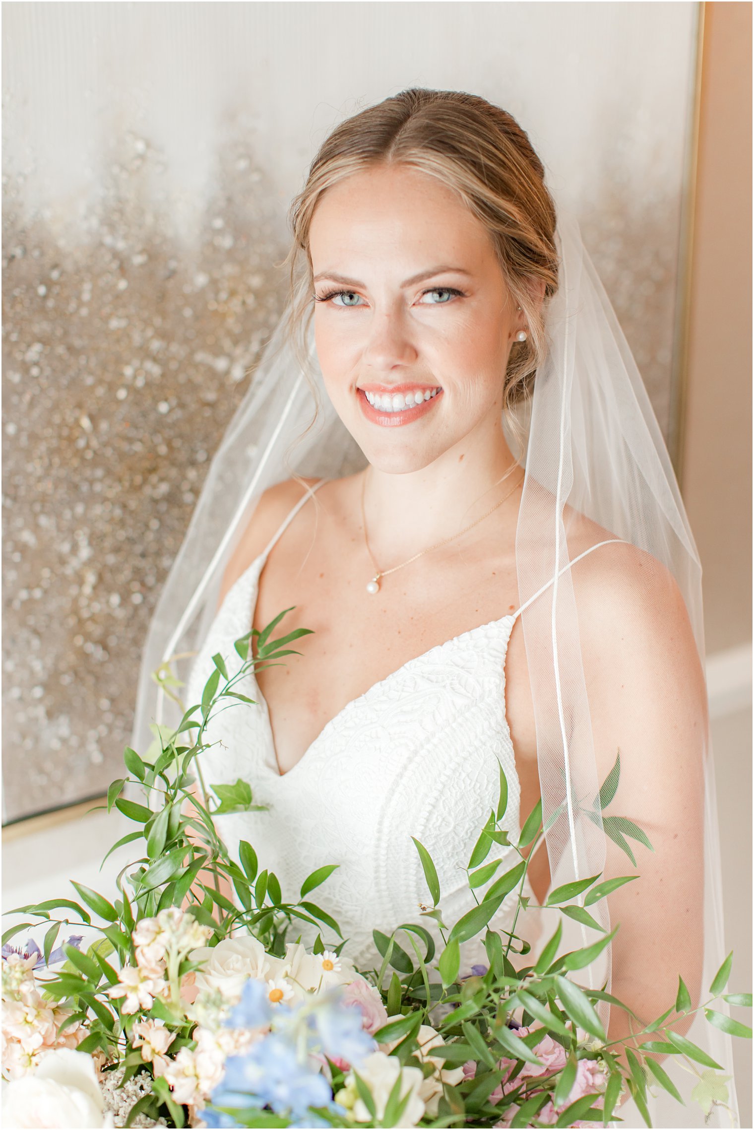 bride holds bouquet and smiles with veil wrapped around shoulders 