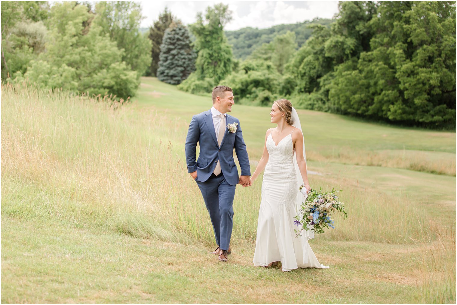 newlyweds hold hands walking in field at Minerals Resort