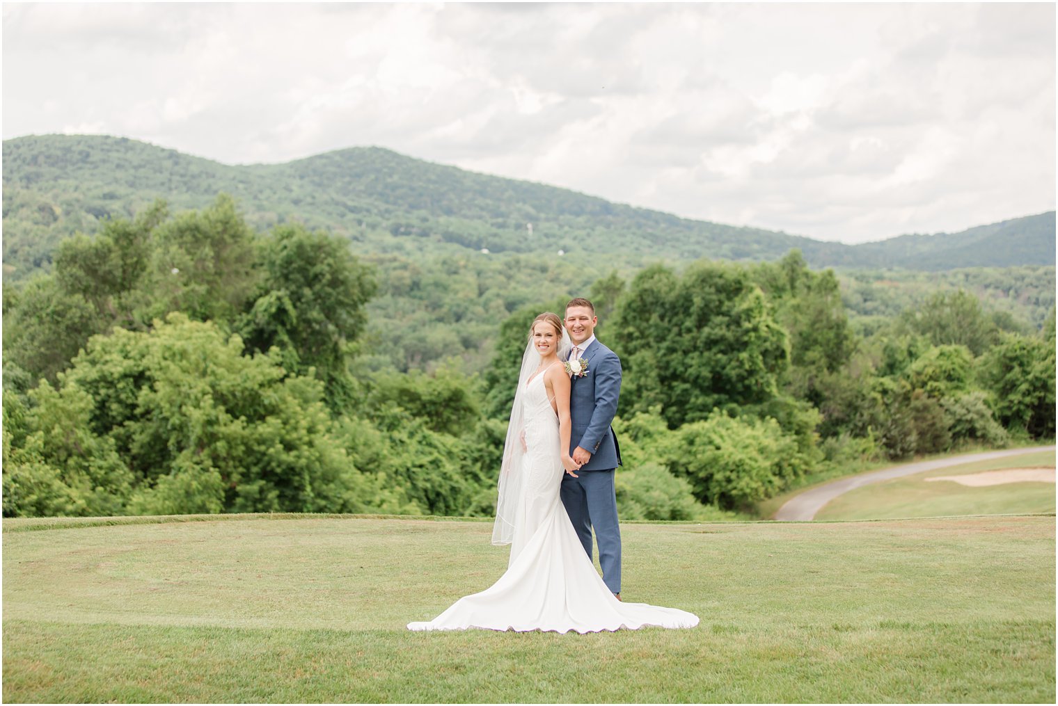 bride and groom pose on green with mountains behind them in Vernon NJ