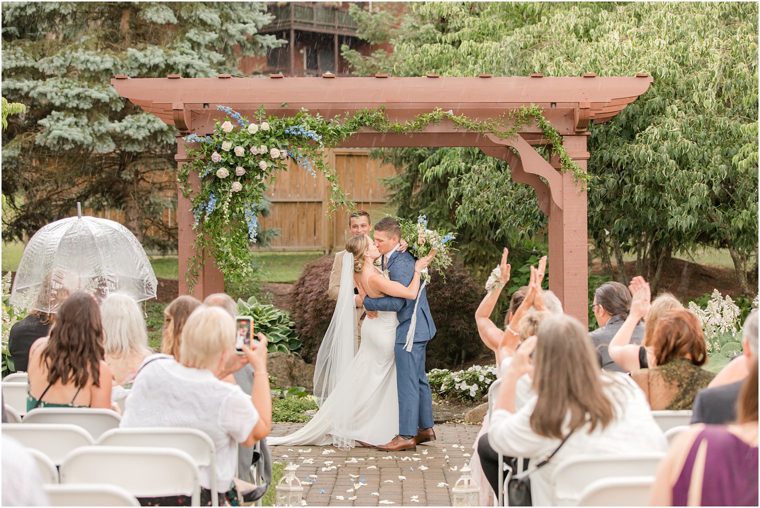 bride and groom kiss at wooden arbor in the rain on wedding day