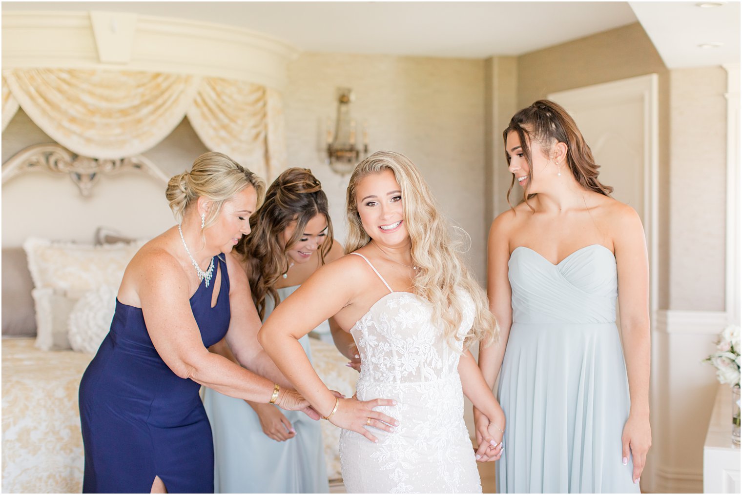 mother and bridesmaids help bride with wedding gown