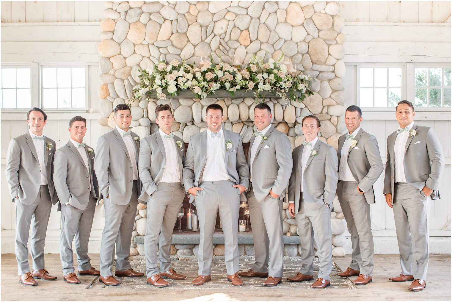 groom poses with groomsmen in grey suits by stone fireplace at Bonnet Island Estate