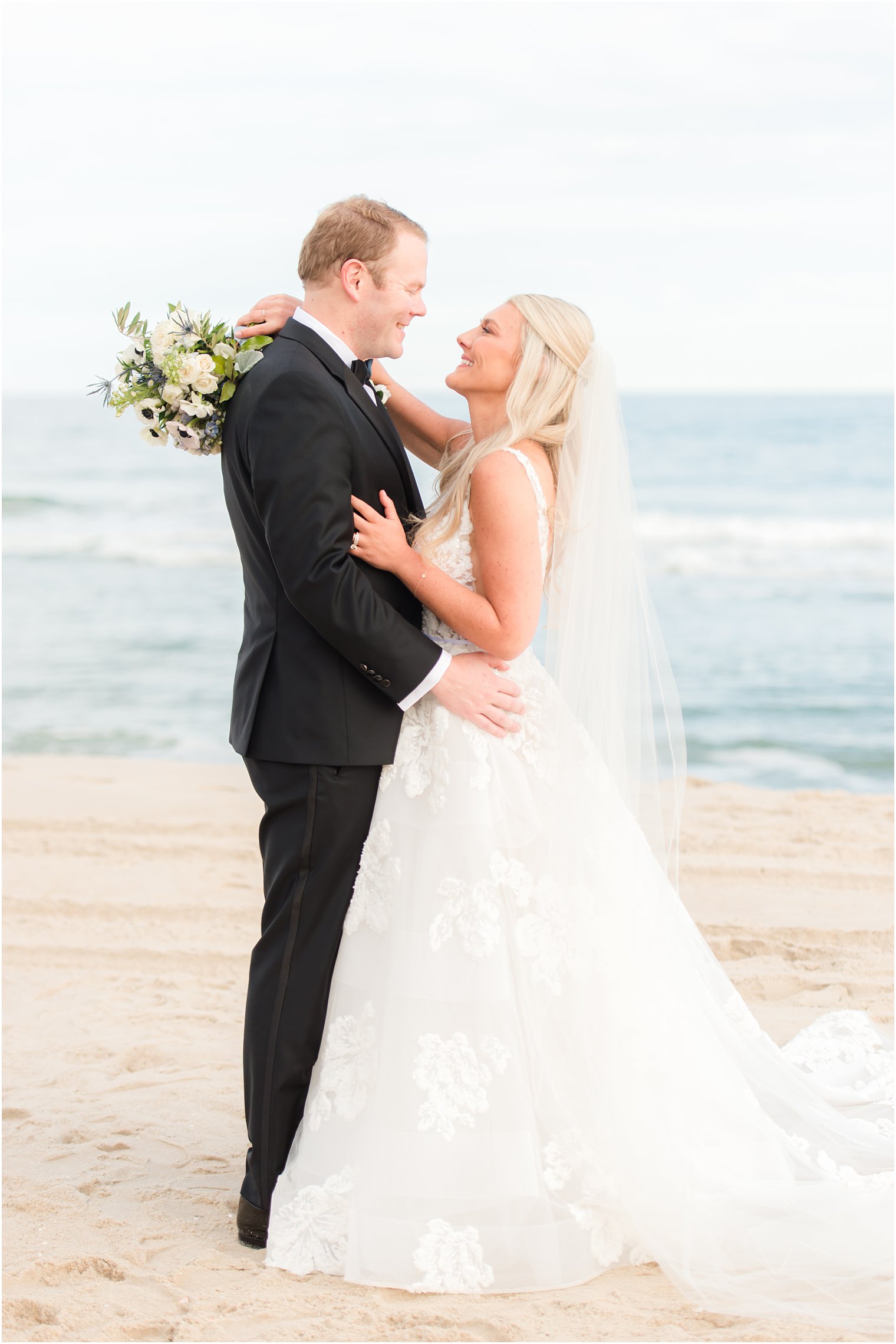 groom hugs bride on beach during fall wedding portraits in New Jersey 