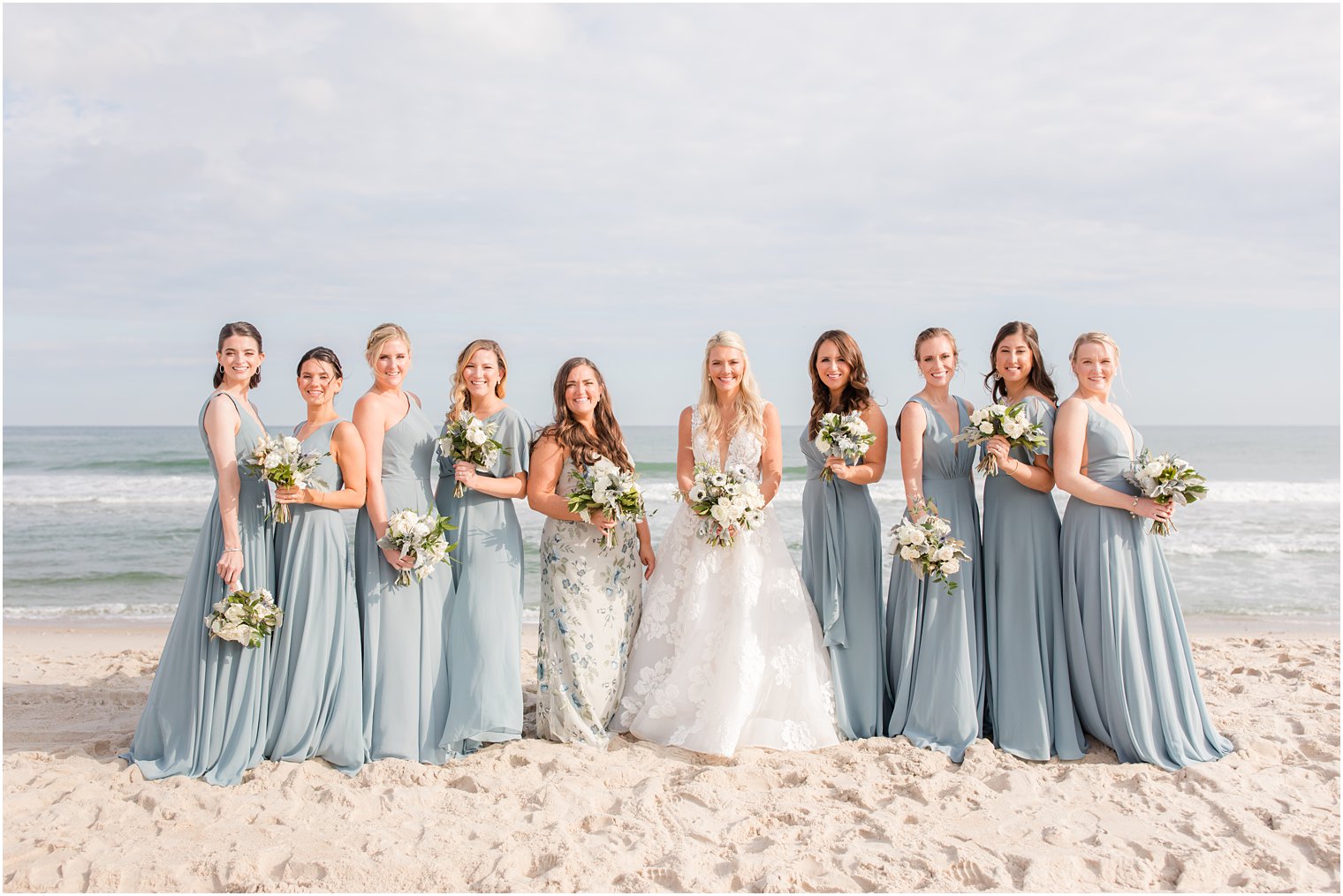bride stands on Brant Beach with bridesmaids in dusty blue gowns 