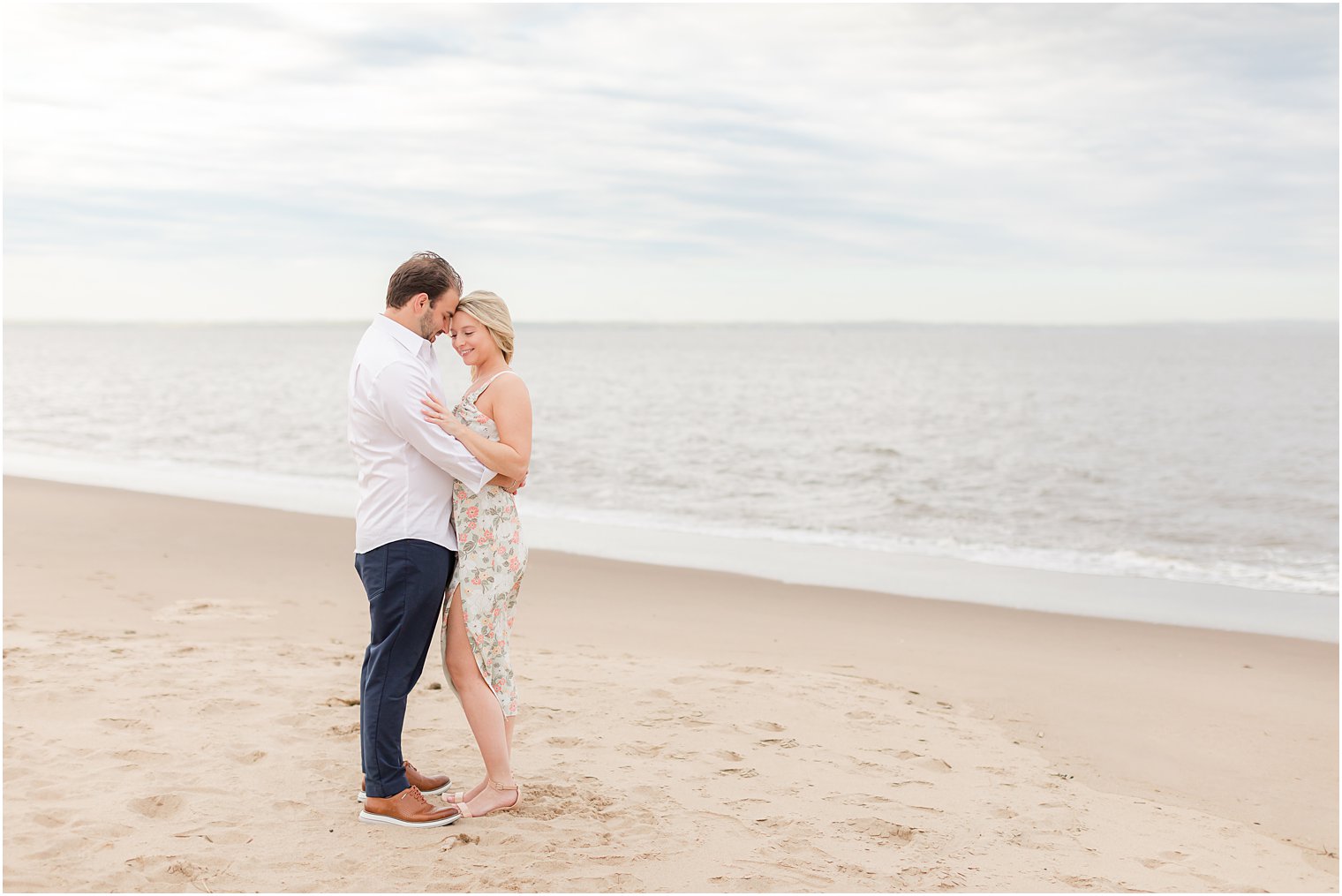 man hugs woman in white dress to him on beach 