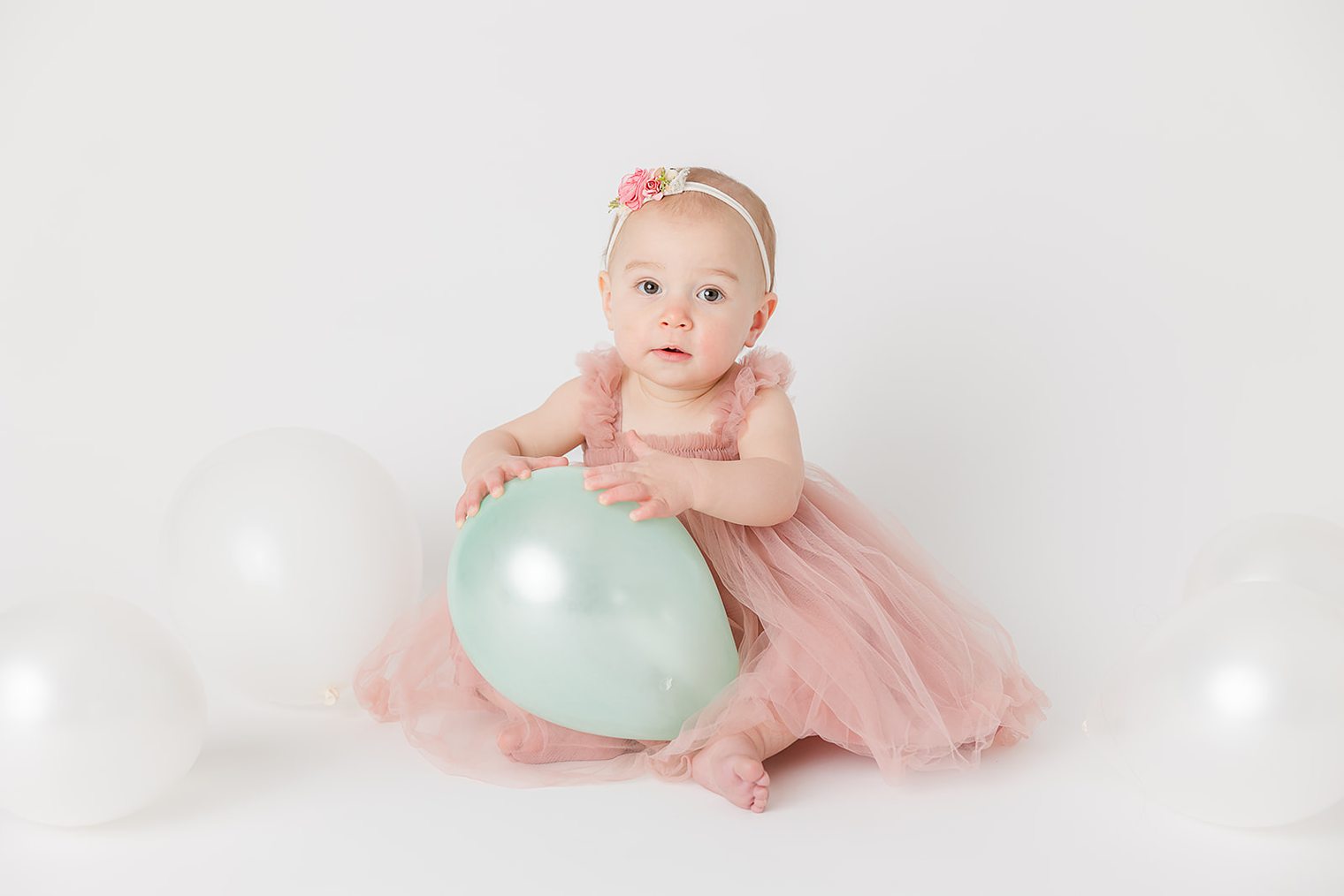 baby girl touching the balloons of her one year session 