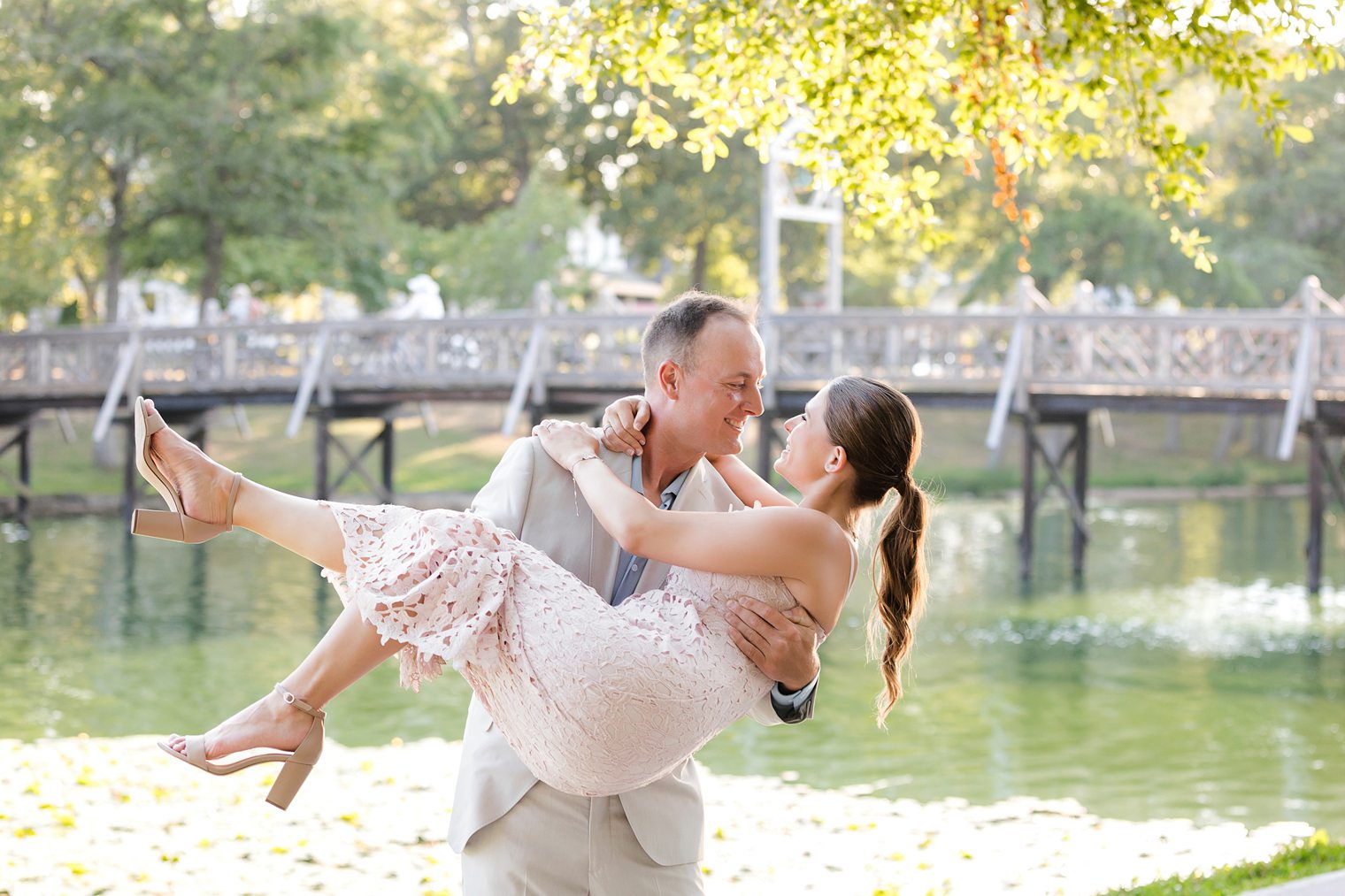 groom holding up his bride while they smile at Spring Lake