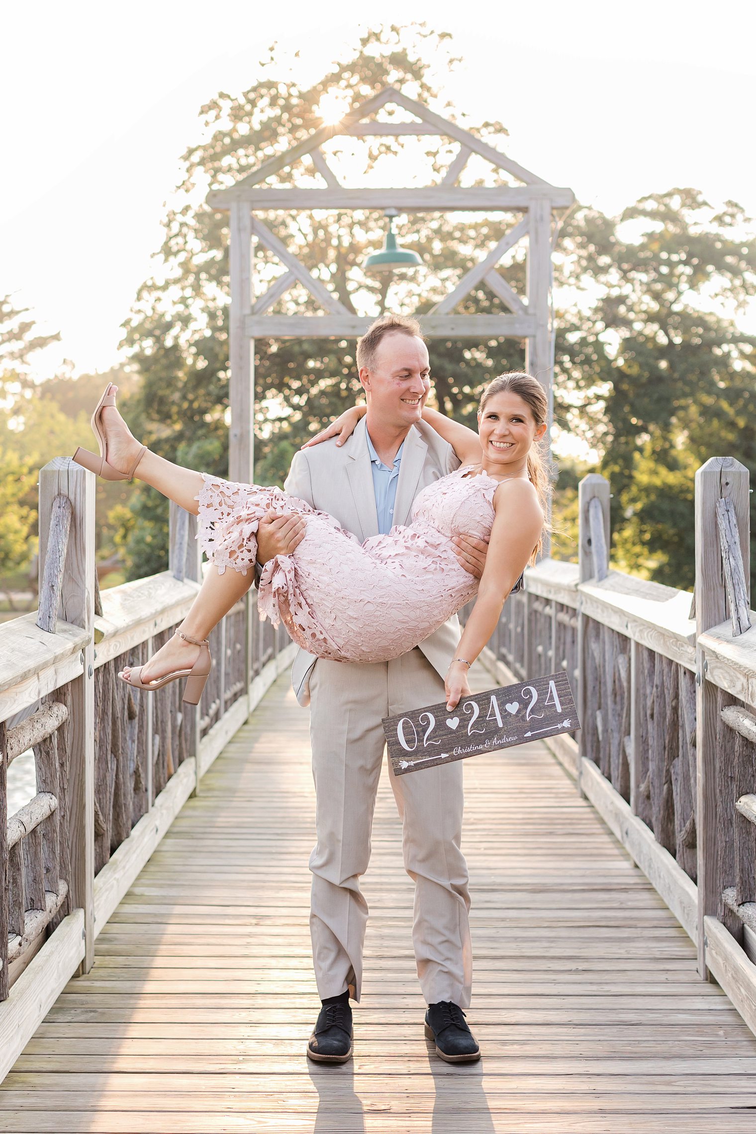 groom holding up his bride and bride holding the save the date sign 