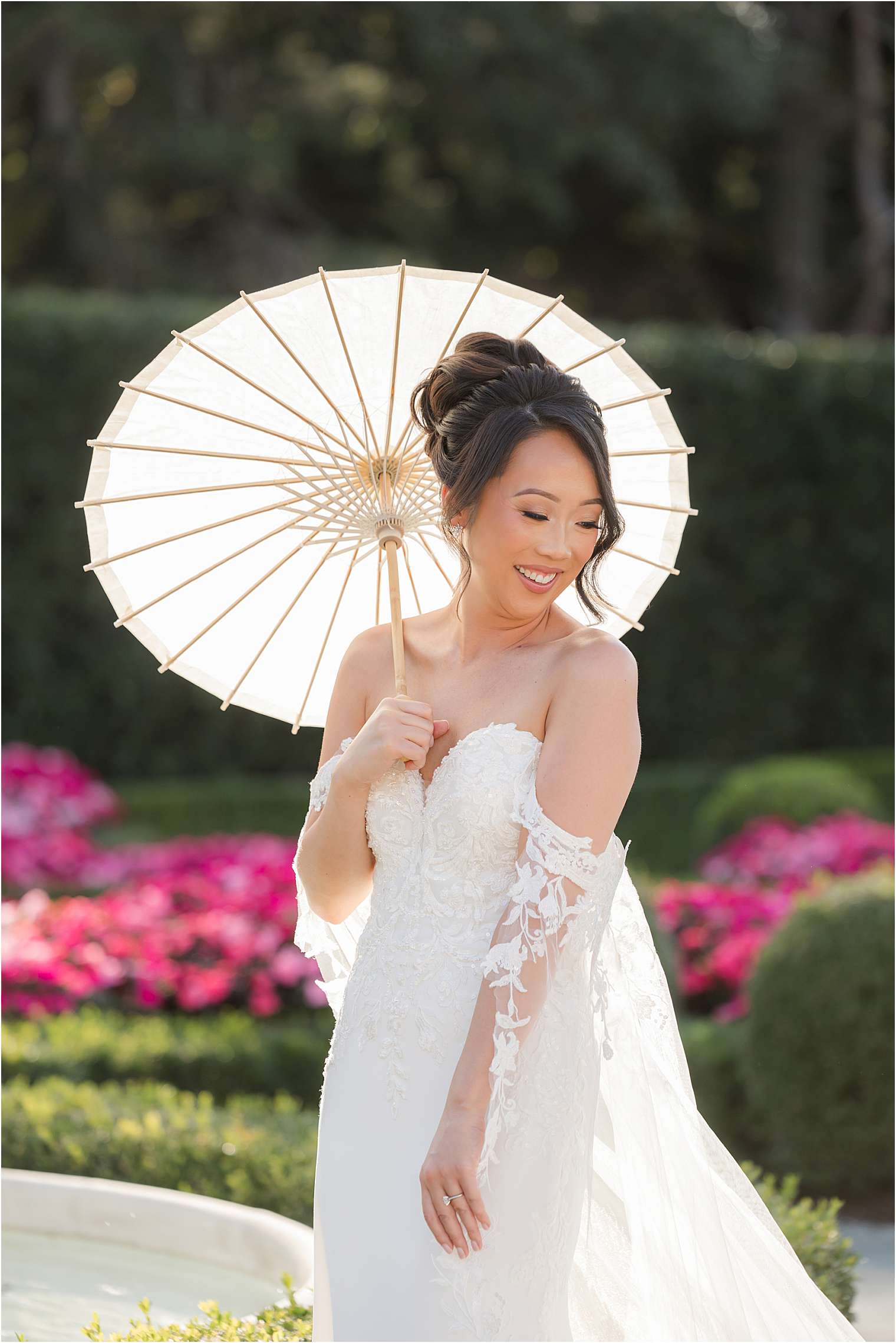 bride smiles while holding a white parasol in a vibrant garden setting